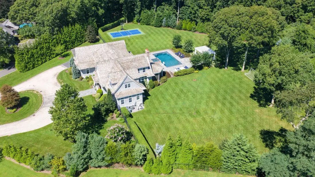 An aerial view shows a large house, swimming pool, and broad lawn.