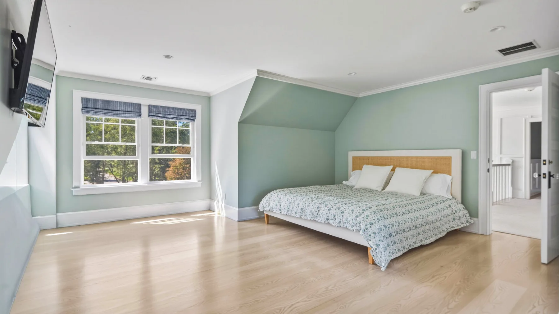A bright bedroom with a bed, pale green walls, and a large window.