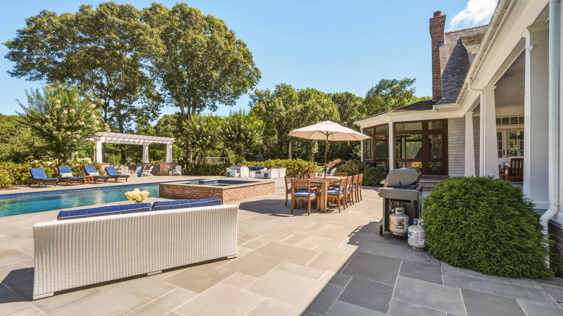 Outdoor patio with seating beside a swimming pool and a white house.