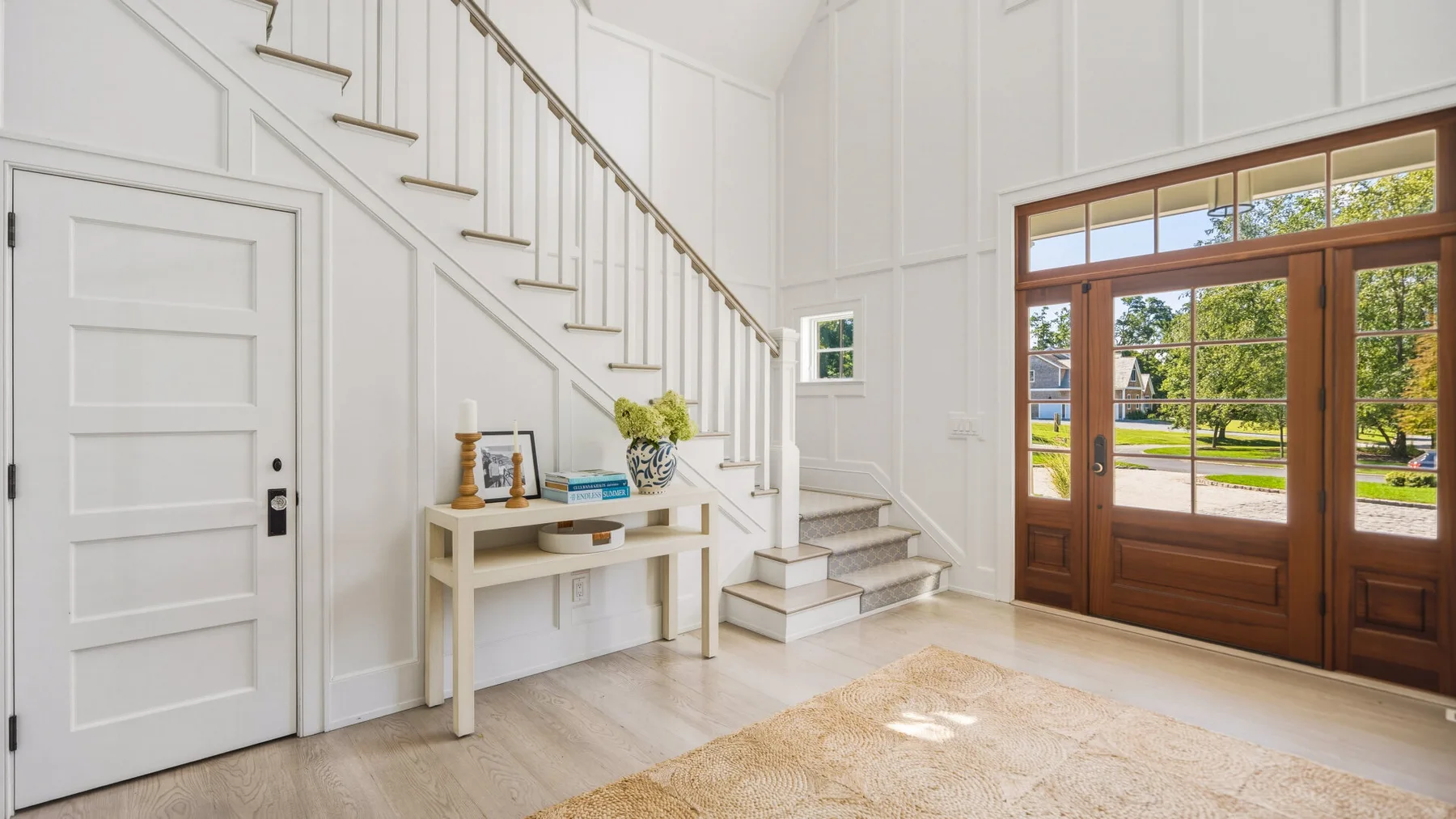 A bright foyer with a staircase, console table, and large glazed entry doors.