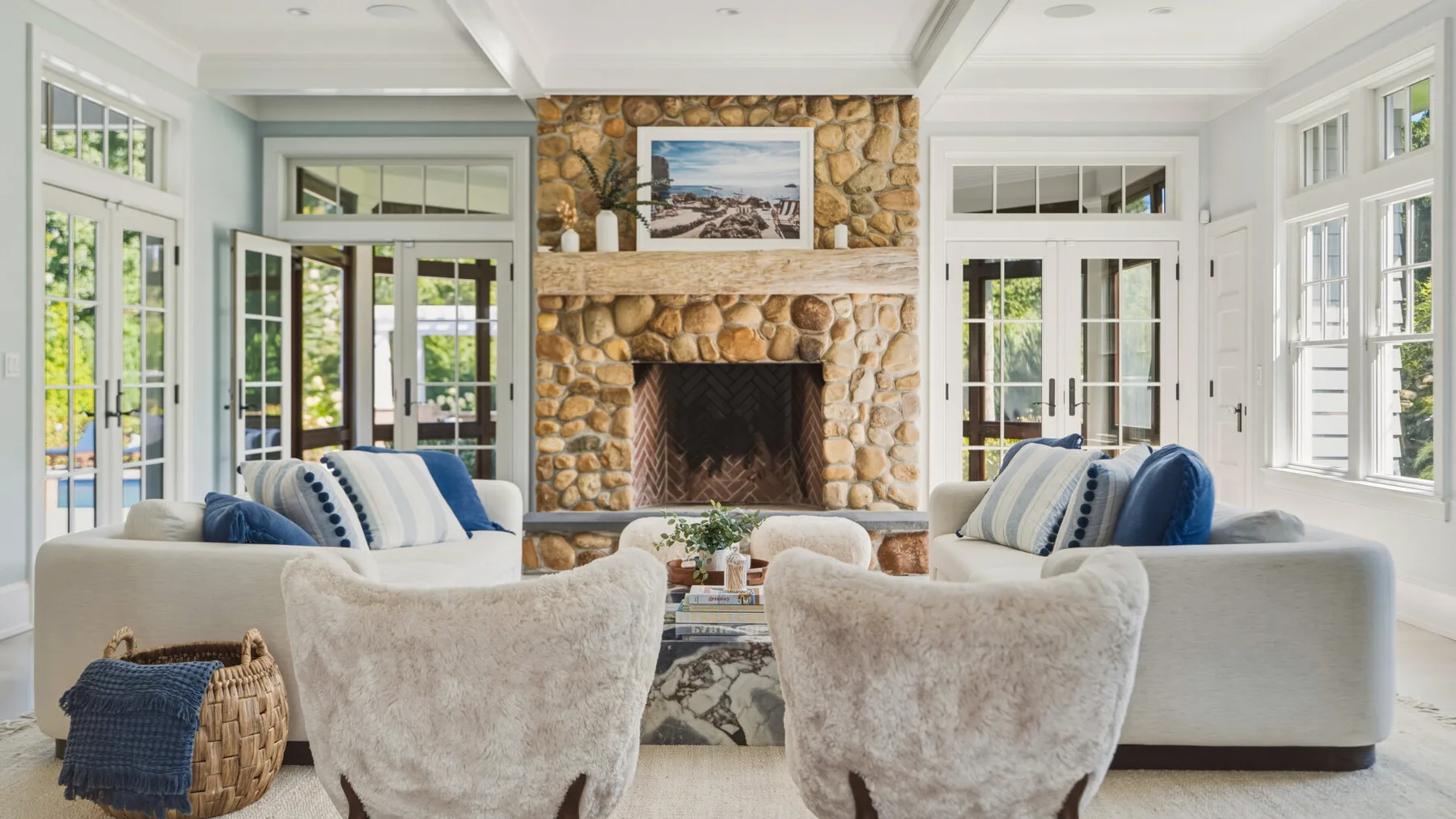 A bright living room with seating arranged around a stone fireplace.