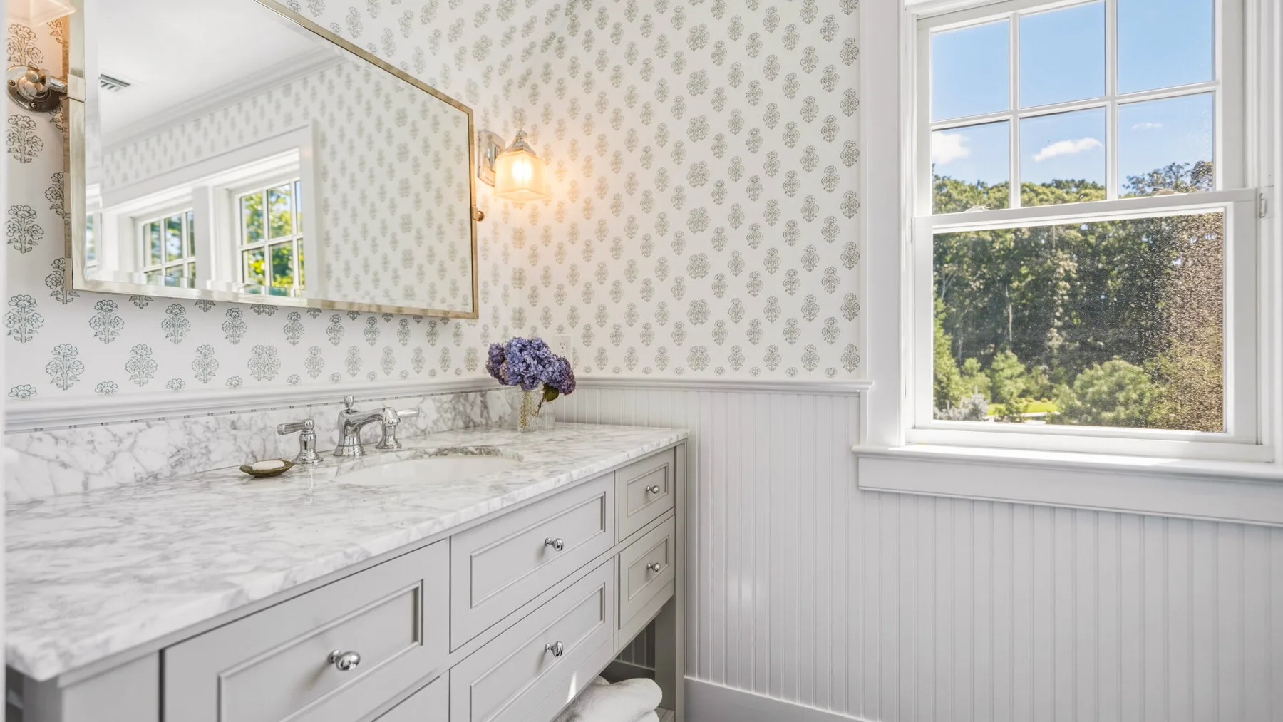 A bright bathroom vanity with a marble countertop and a large window.