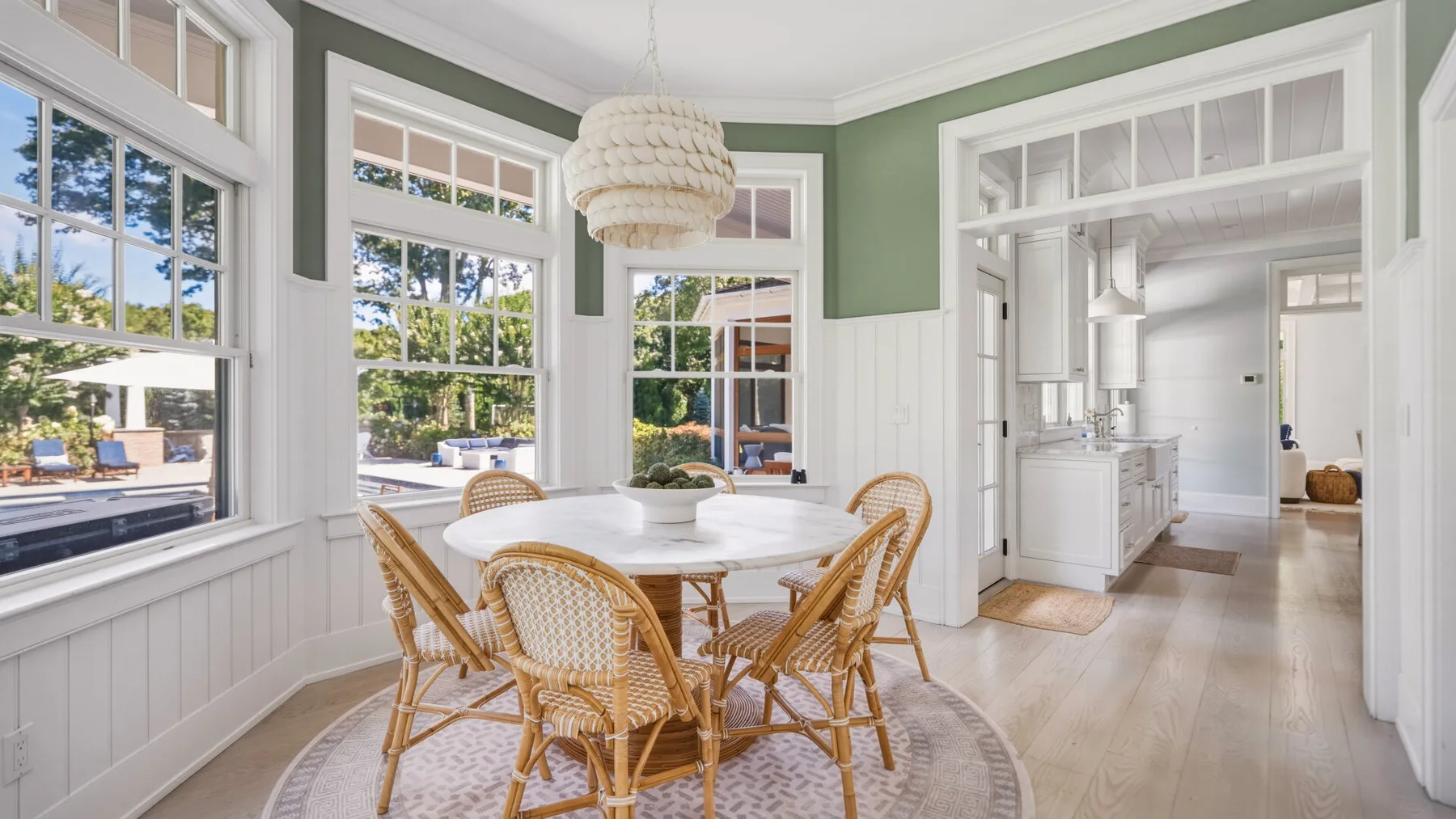 A bright dining area has a round table and woven seating beside large windows.