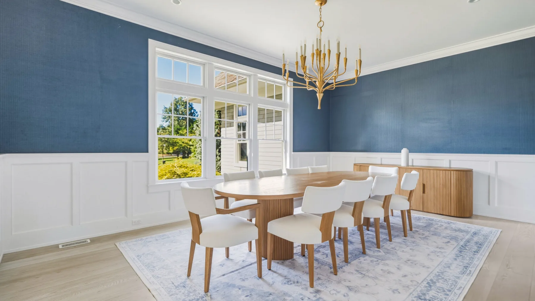 A dining room with a long table and chairs beneath a chandelier.