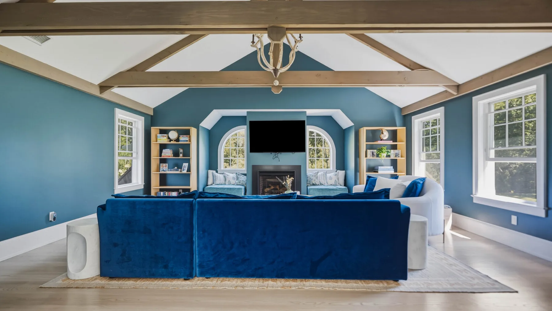 A blue living room with a large sectional facing a fireplace and television.