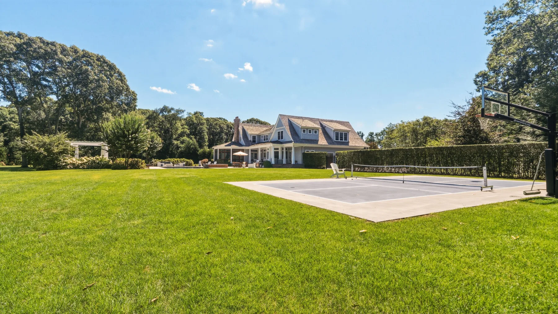 A large house stands beyond a lawn and outdoor basketball court.