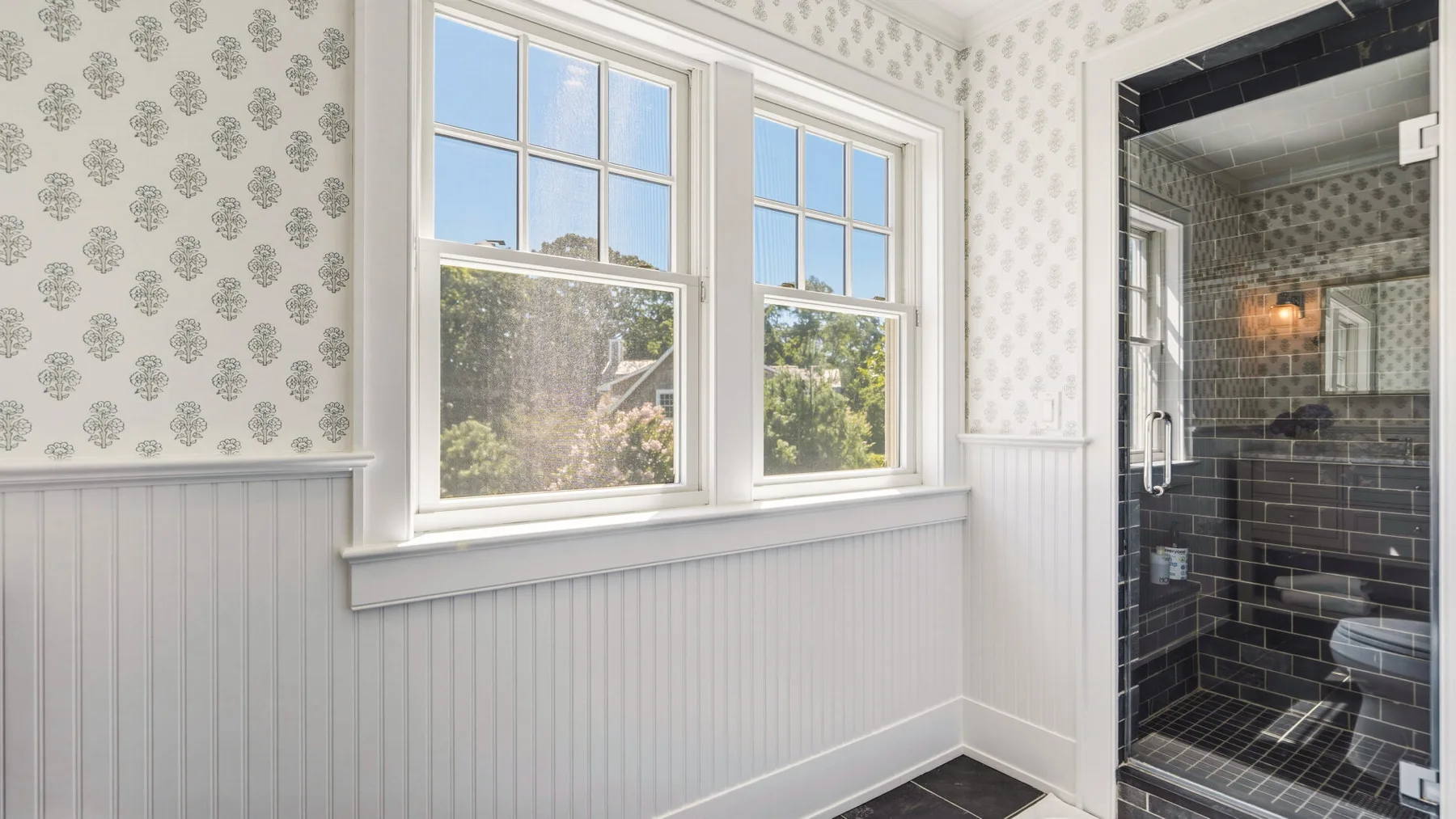 A bright bathroom with large windows beside a dark tiled shower.