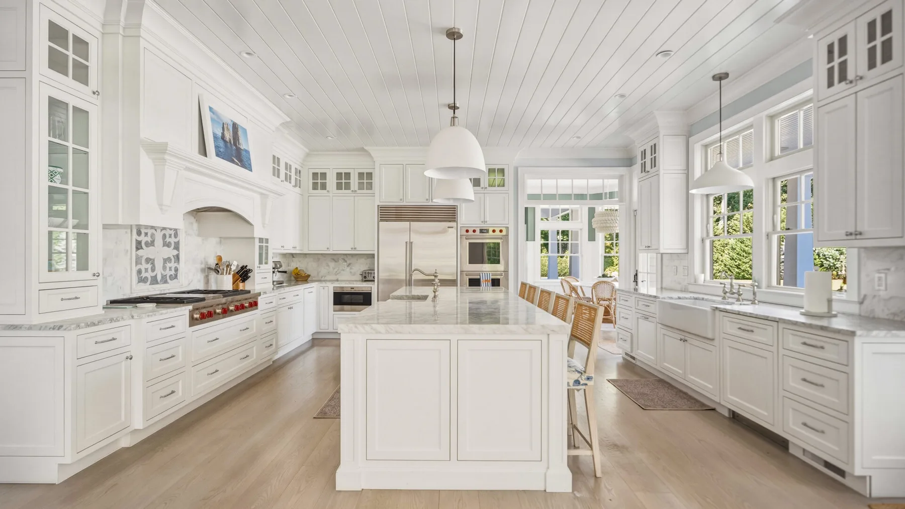 A bright white kitchen with a central island and large windows.