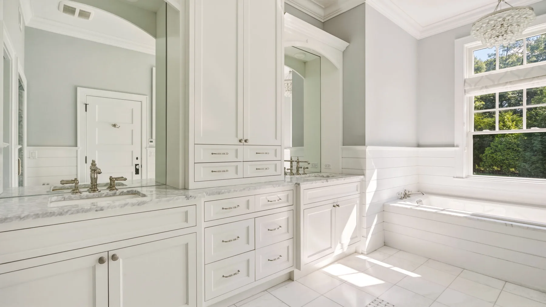A bright bathroom with a long vanity, mirrors, and a large window.