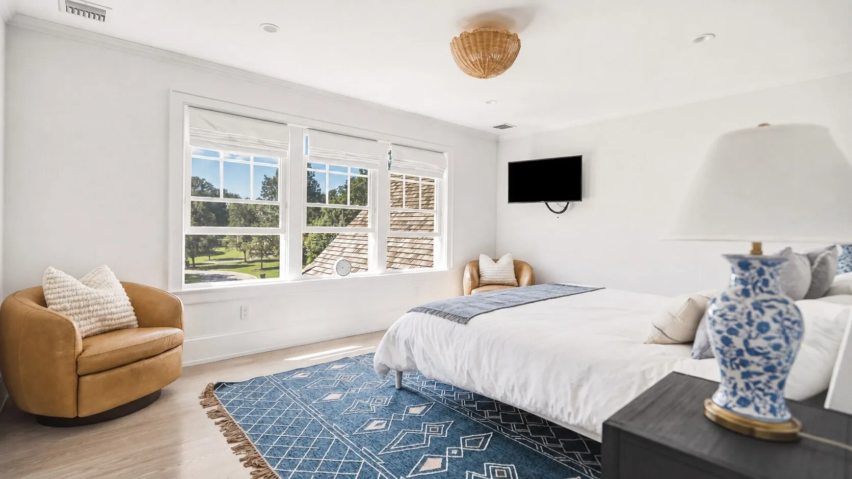 A bright bedroom with a large bed, windows, and a blue patterned rug.