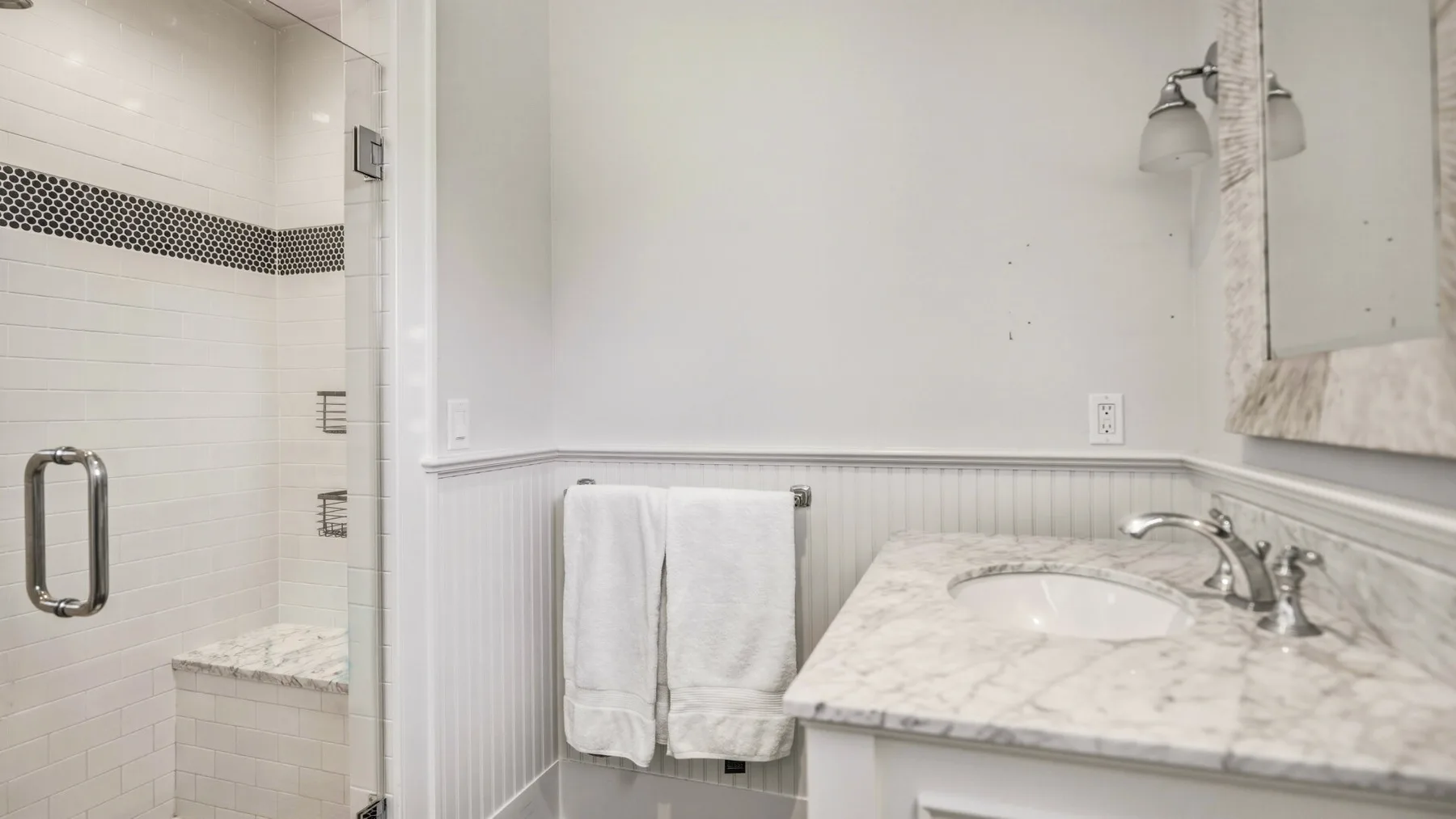A bathroom vanity with a sink and towels beside a tiled shower.