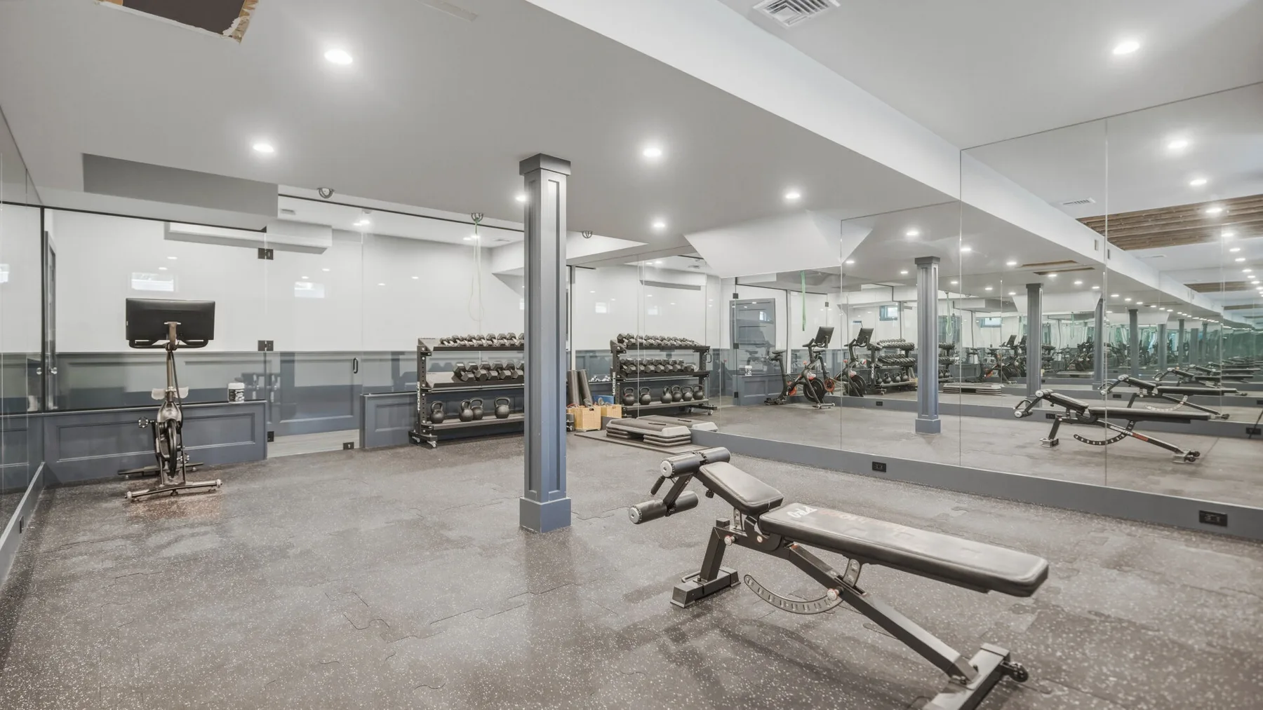 A gym with weight racks, exercise machines, and a large mirrored wall.