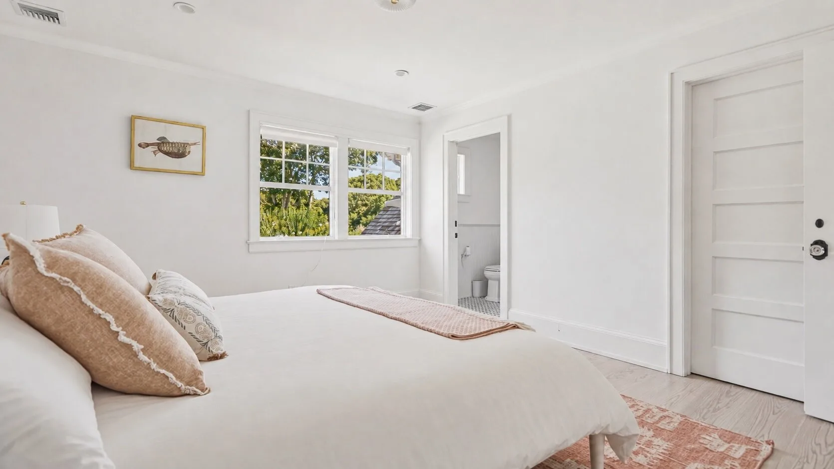 A bright bedroom with a neatly made bed and windows overlooking greenery.