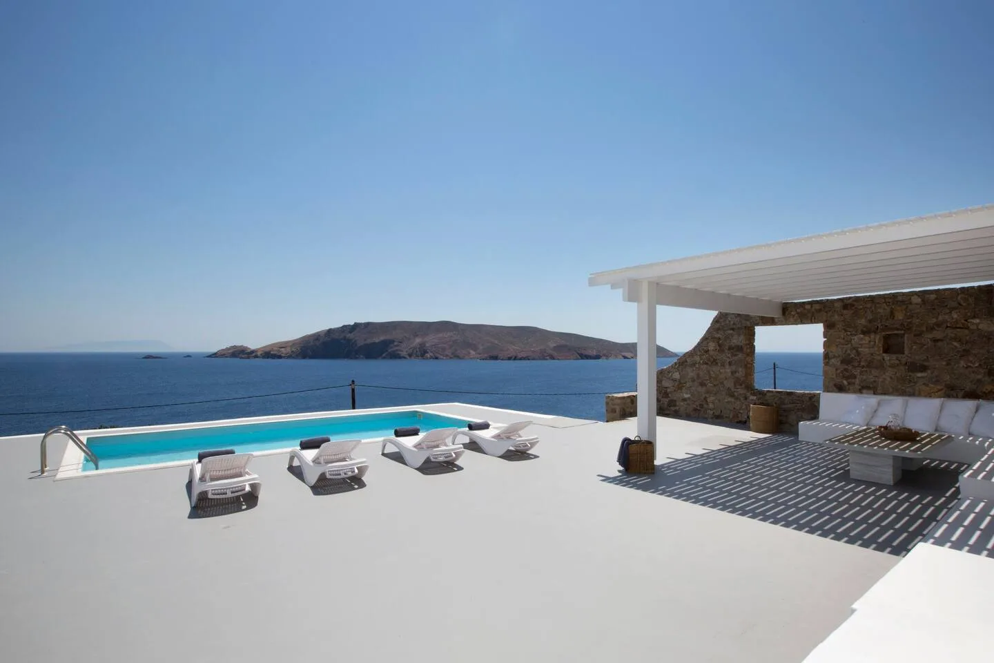 A seaside terrace with a swimming pool and lounge seating overlooking the water.