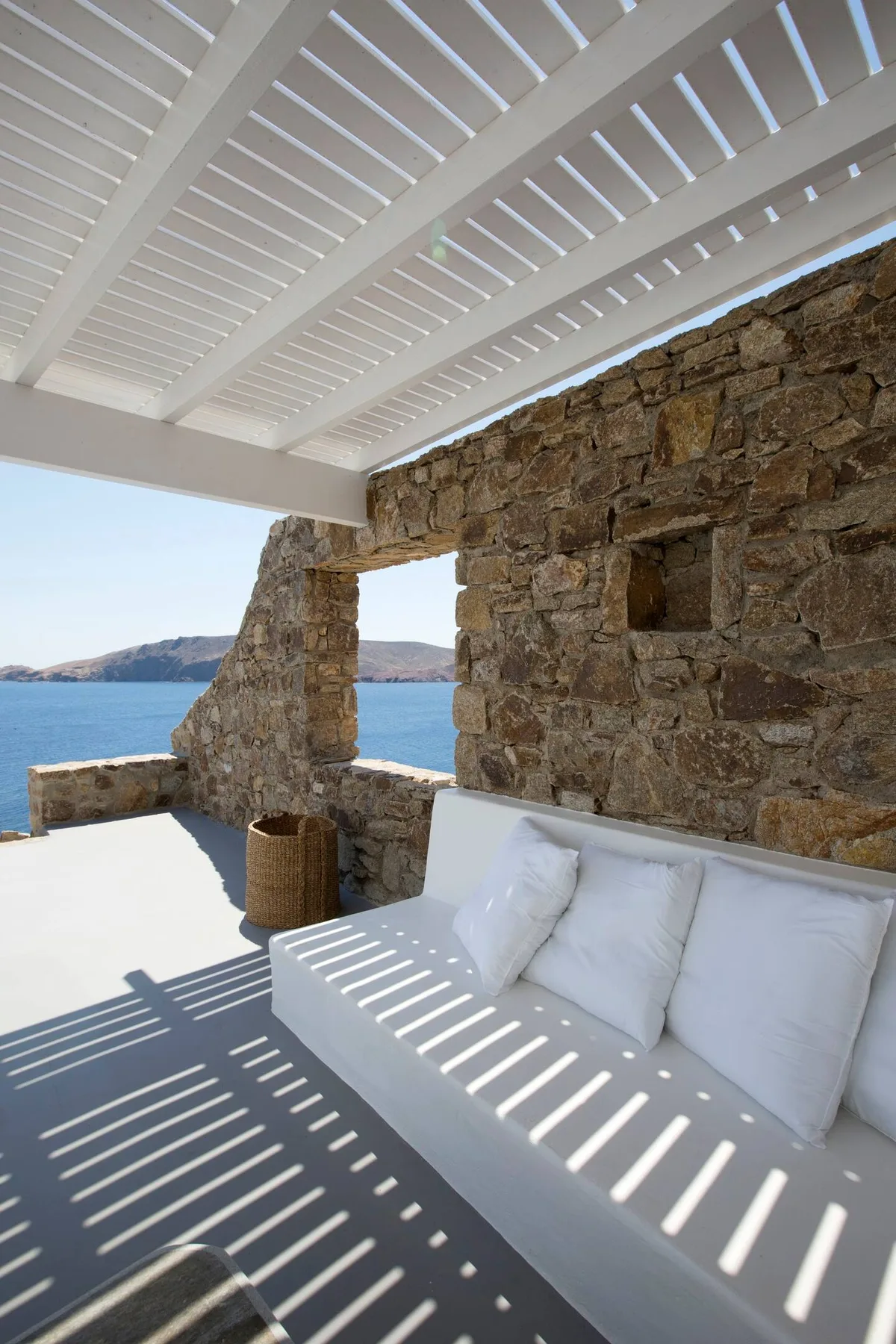 A covered outdoor seating area overlooks the sea beside a stone wall.