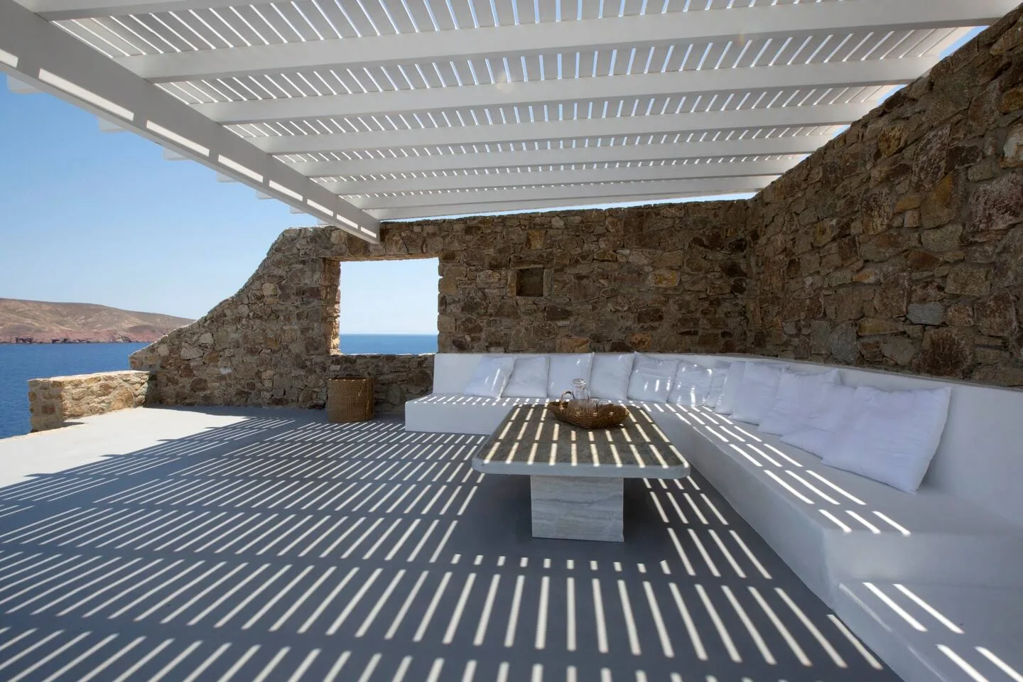 A covered outdoor lounge with white seating and a view of the sea.