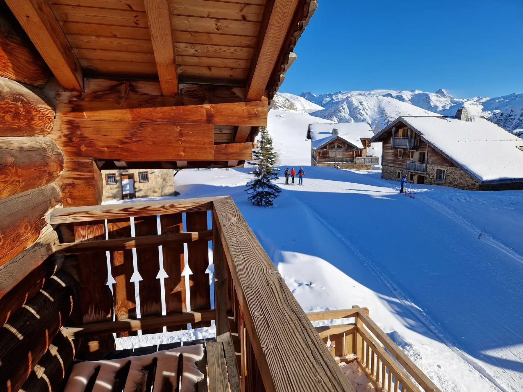 A wooden balcony overlooks snow-covered chalets and a mountain range.