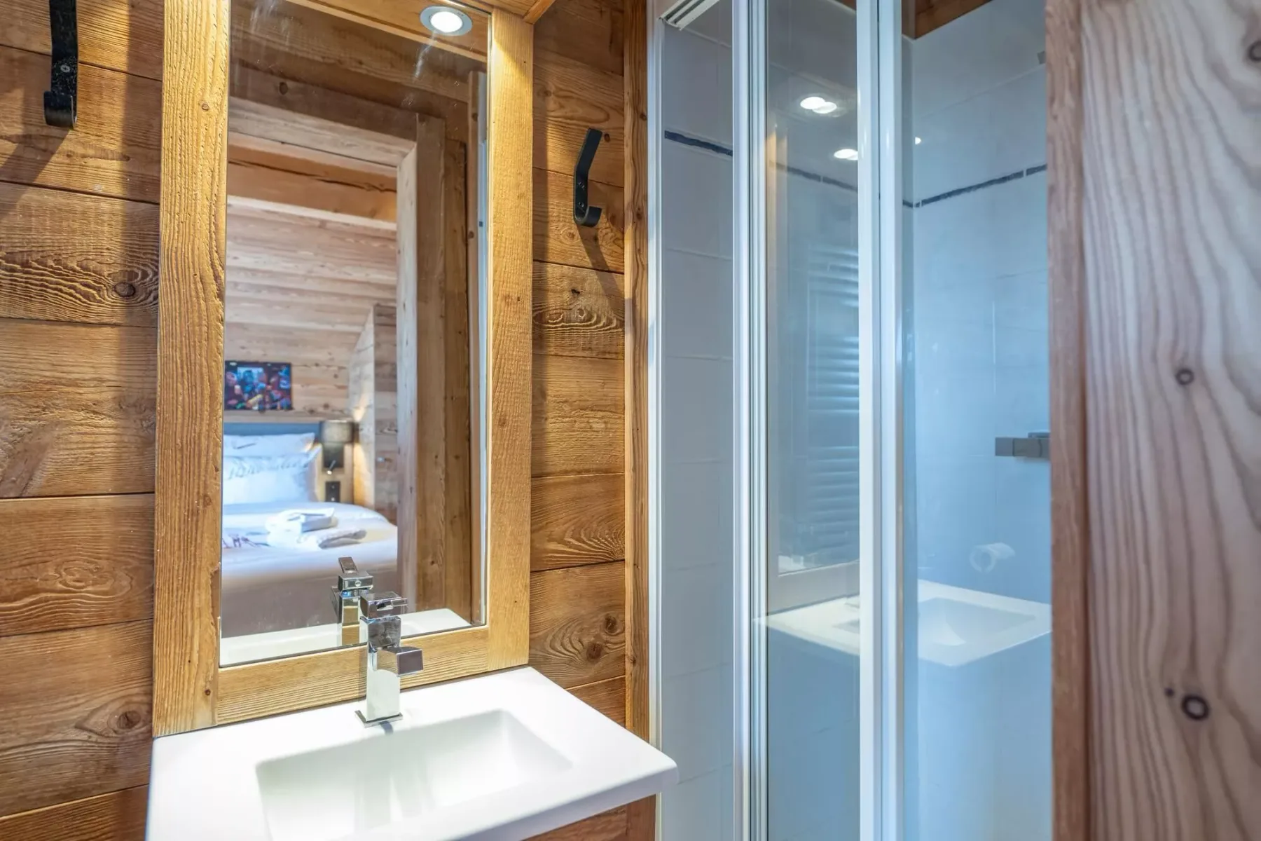 A wood-paneled bathroom with a sink, mirror, and glass shower.