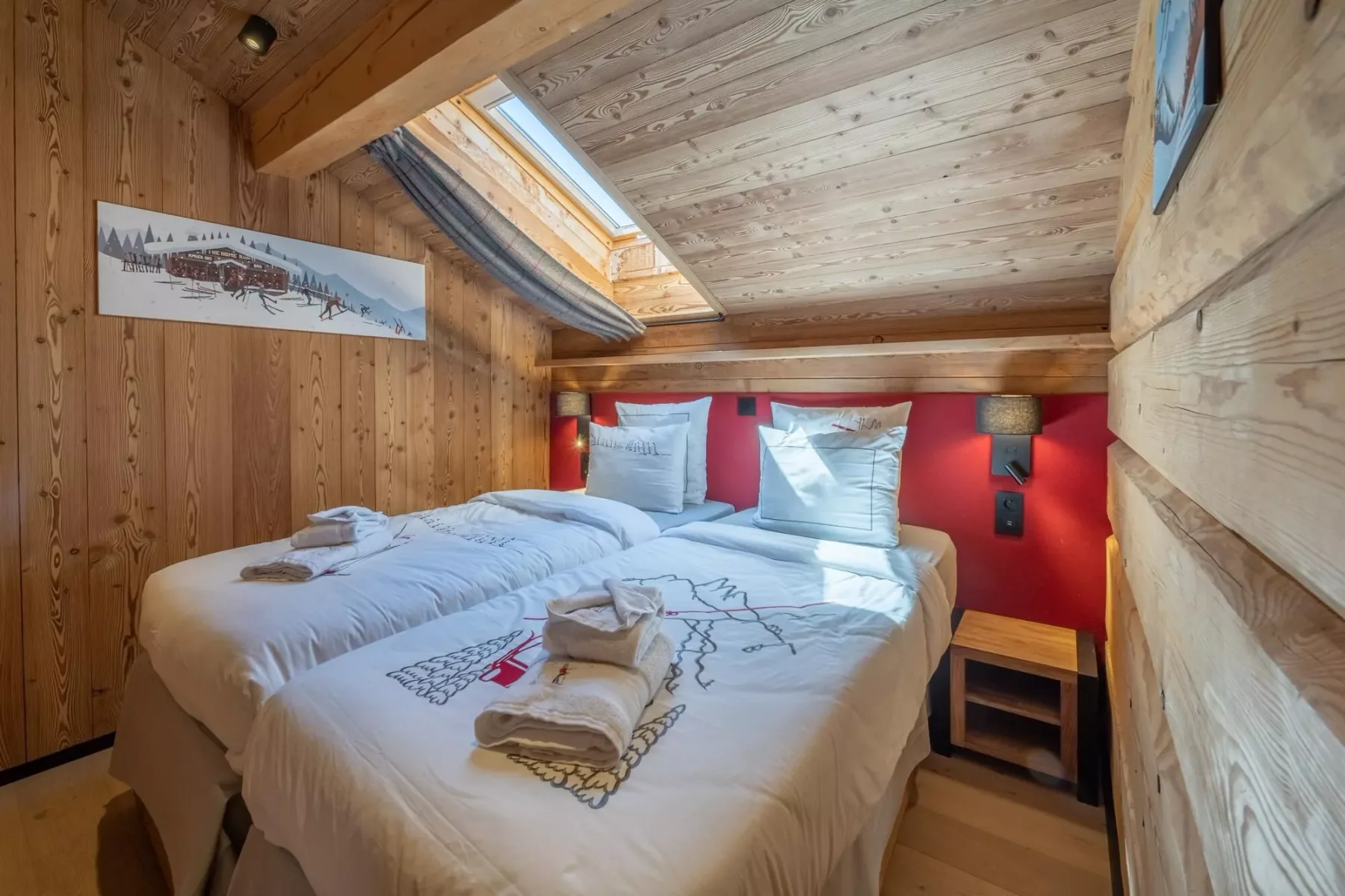 A bedroom with two beds beneath a sloped wooden ceiling and skylight.