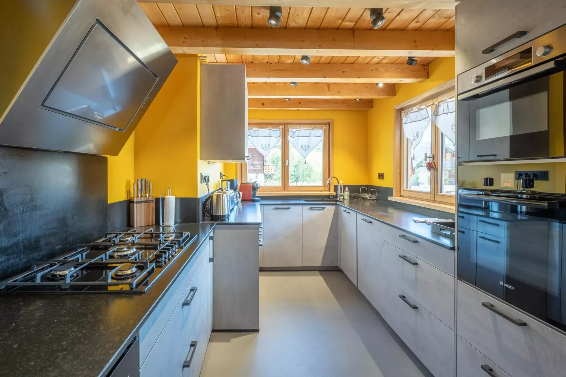 A bright kitchen with gray cabinets, dark counters, and windows along the back and side.