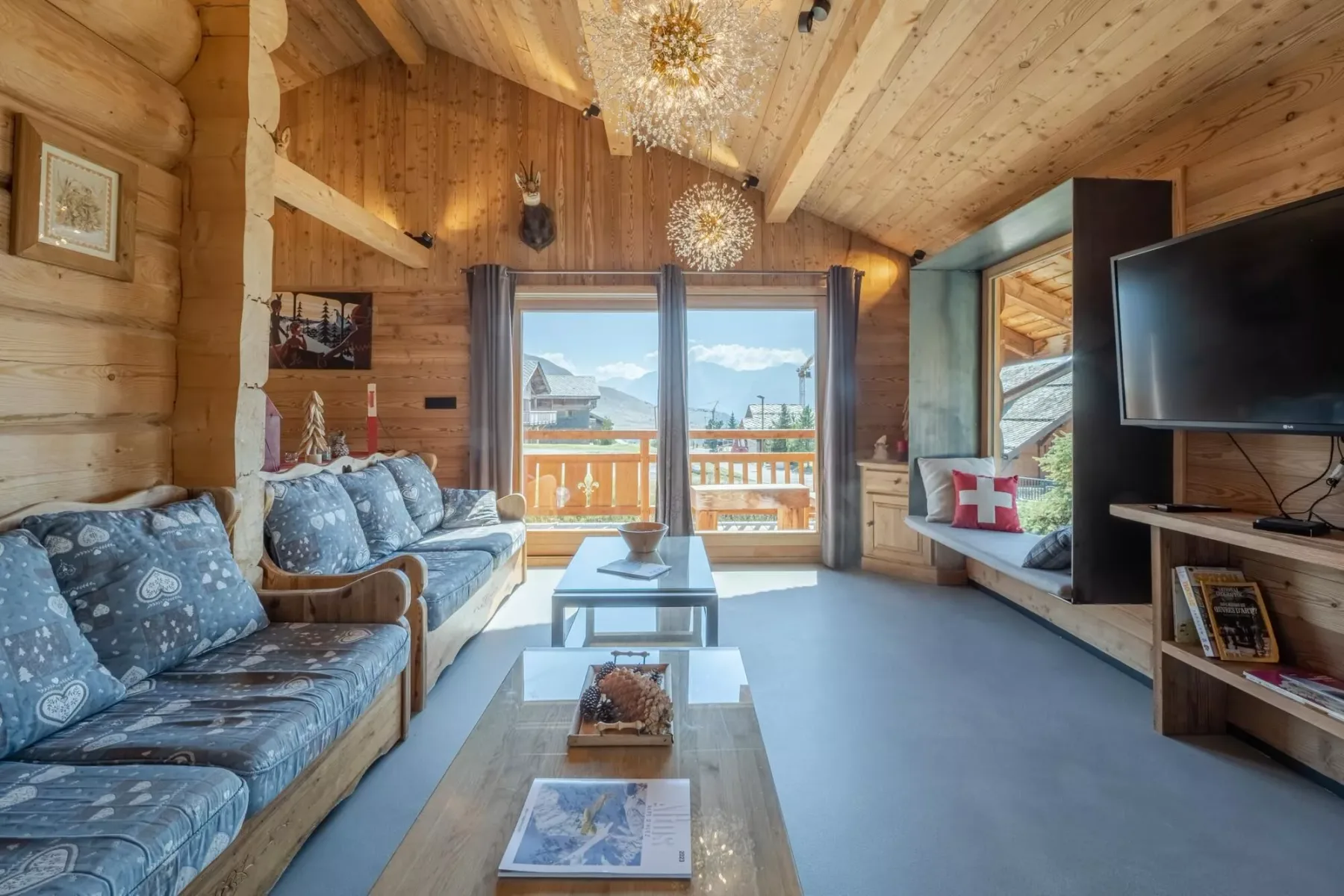 A wood-paneled living room with seating, a television, and glass doors opening onto a balcony.