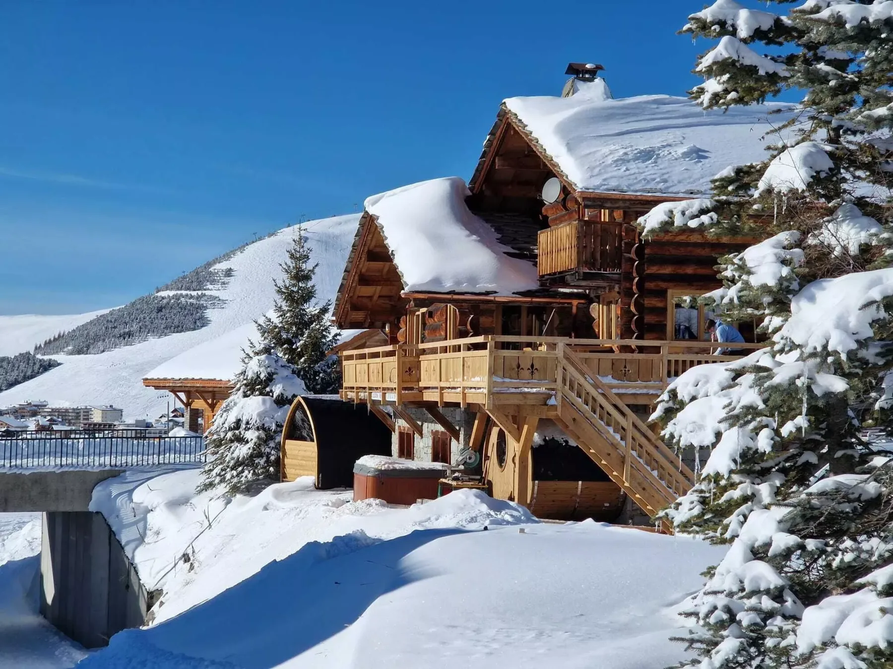 A snow-covered log cabin with wooden balconies sits among evergreen trees.