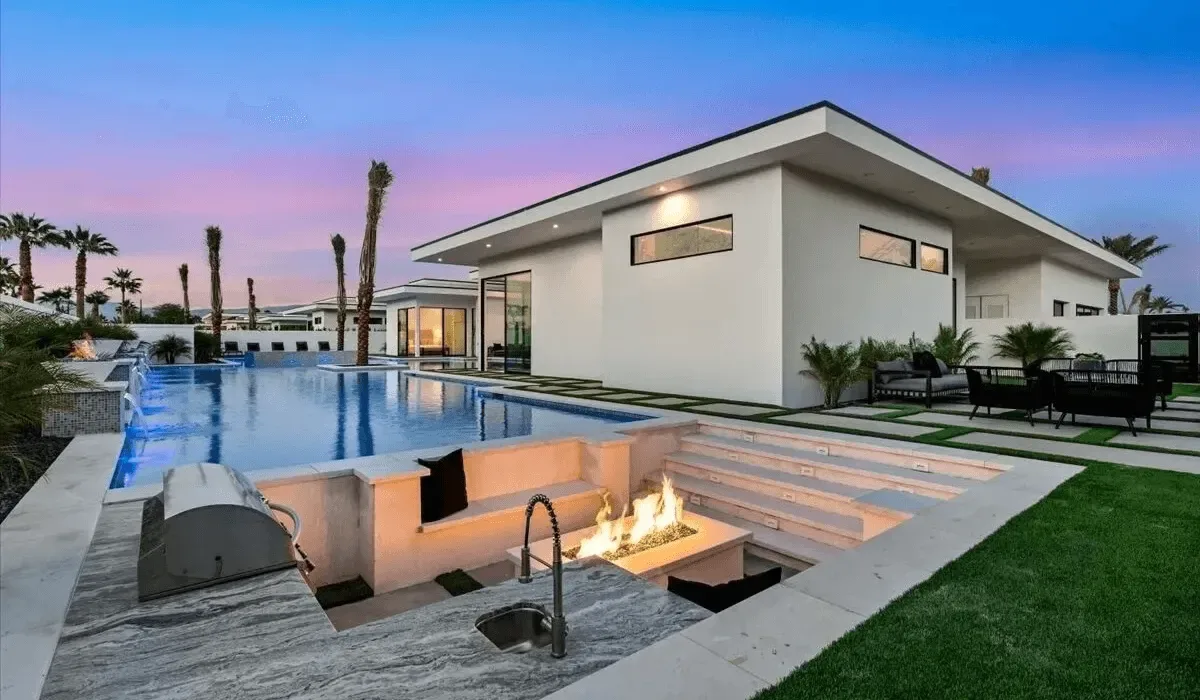 Casa moderna junto a una piscina, con una fogata encendida en primer plano.