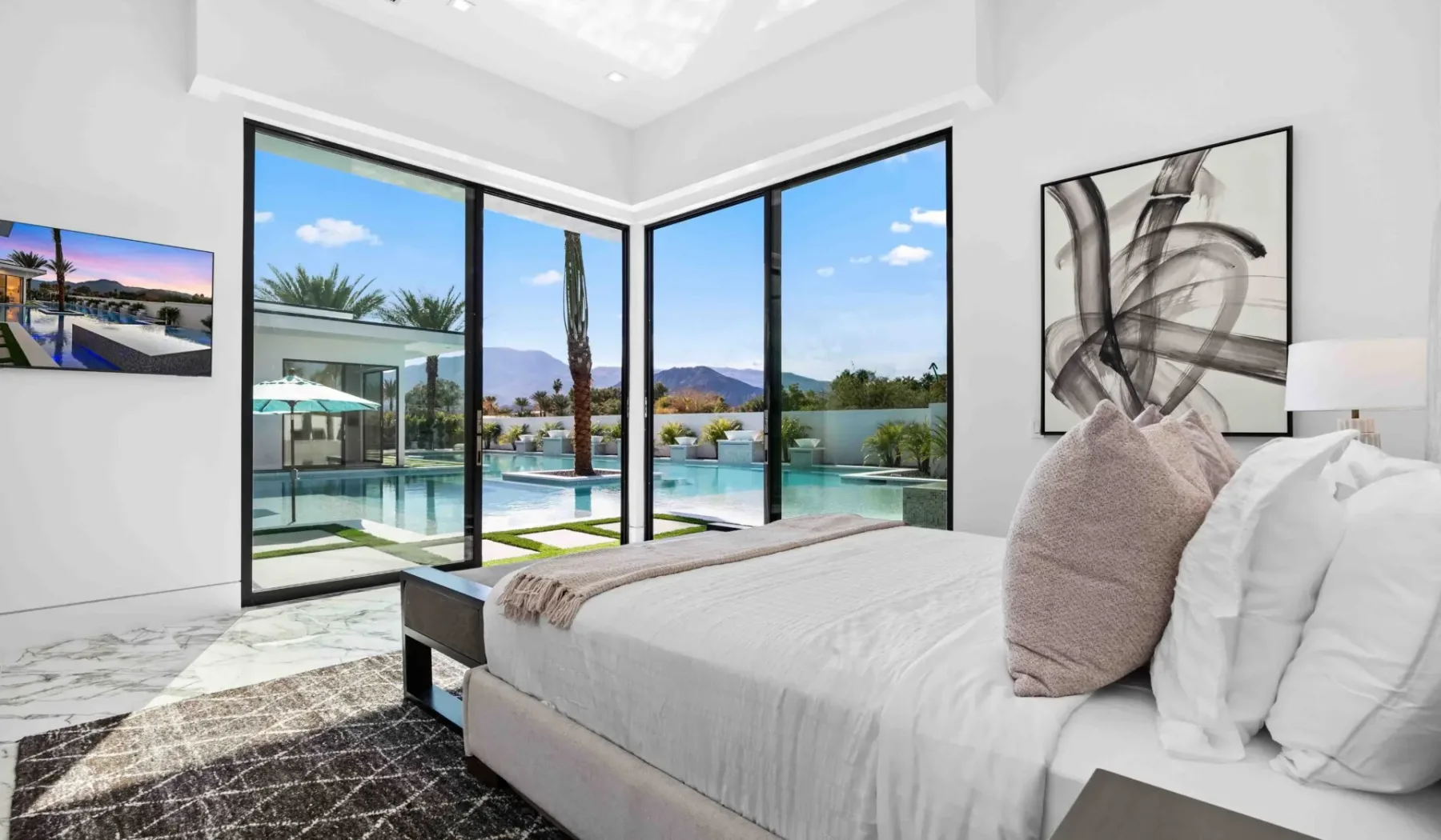 A bright bedroom with a bed beside large windows overlooking a pool.