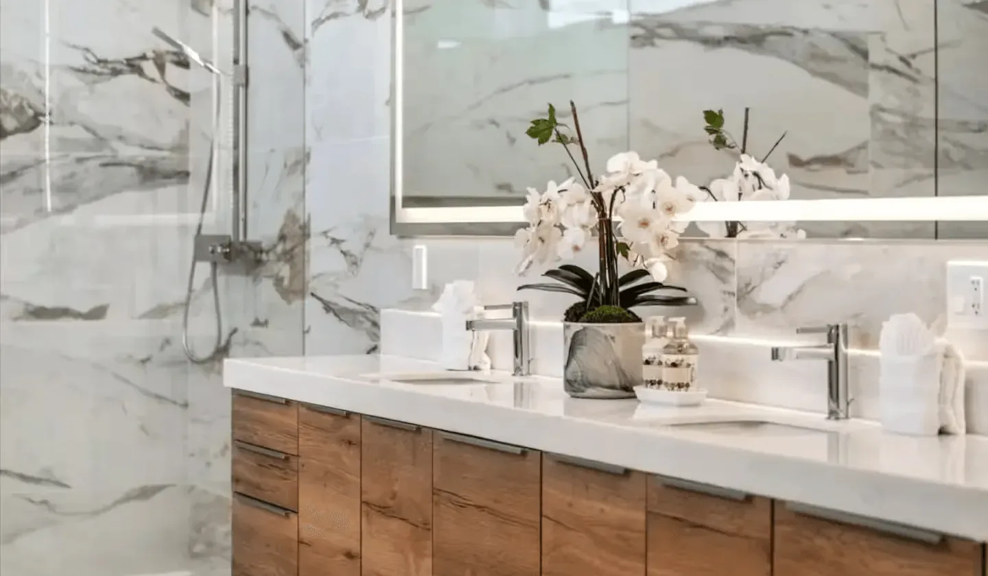 A bathroom vanity with a white countertop, flowers, and marble-patterned walls.