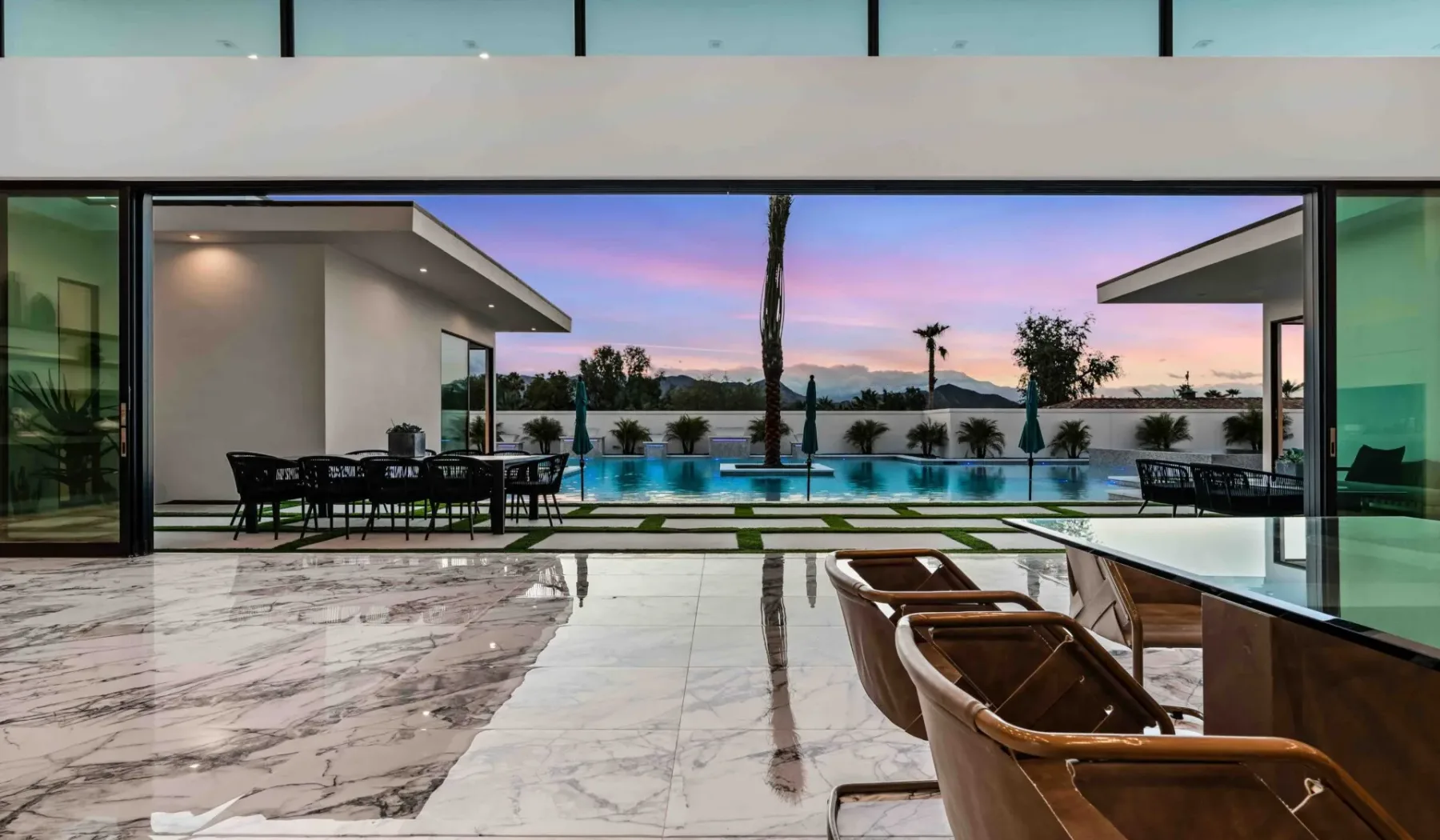 A modern open-air dining area overlooks a swimming pool at sunset.