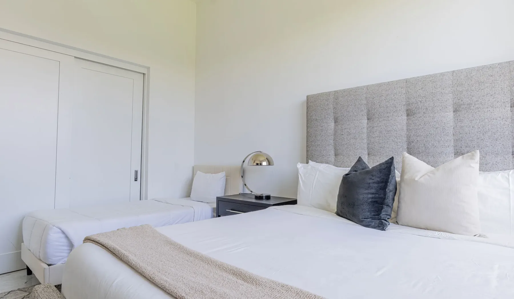 A bedroom with two beds, white bedding, and a gray upholstered headboard.