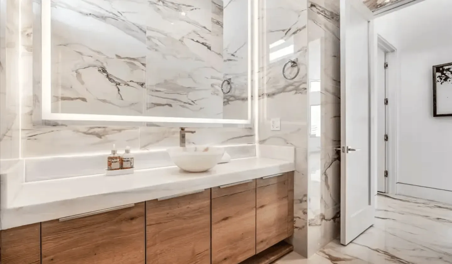 A bright bathroom with a wide vanity, vessel sink, and marble-patterned walls.