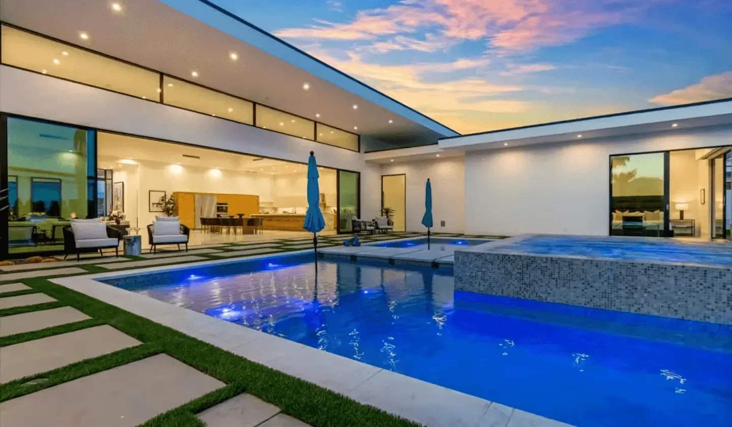 A modern courtyard with a blue swimming pool beside a glass-fronted living area.