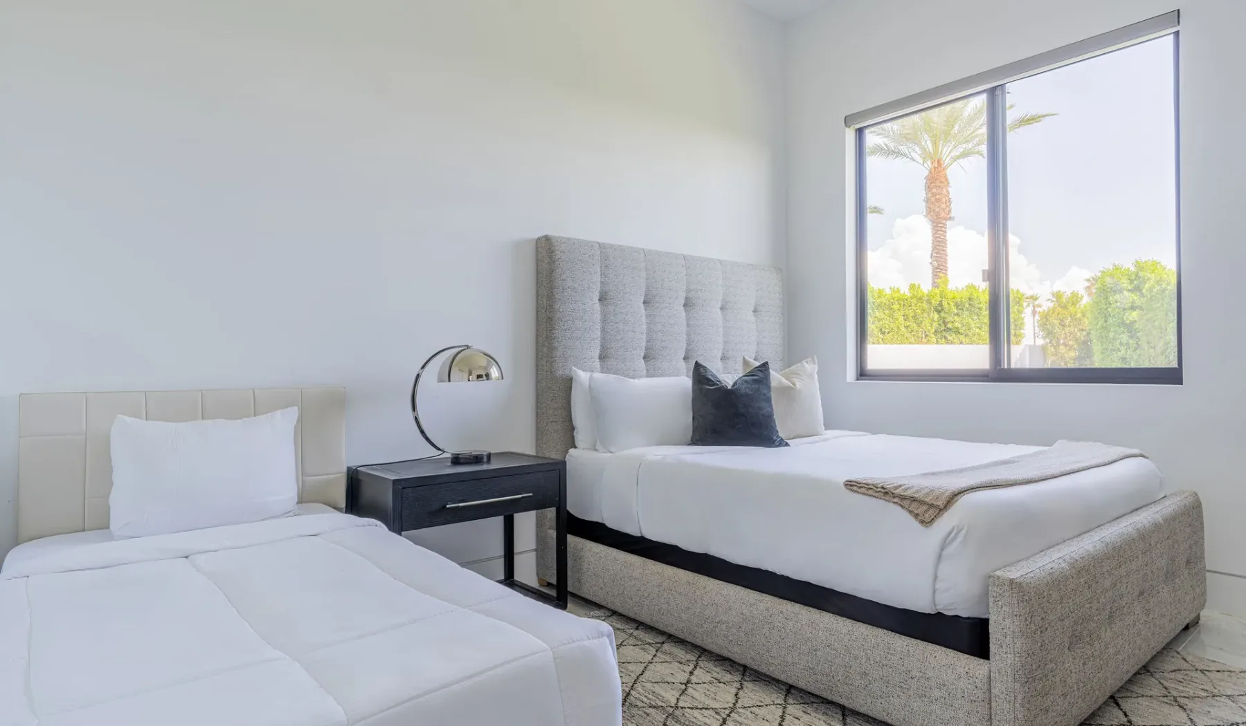 Bedroom with two beds and a window overlooking palm trees.