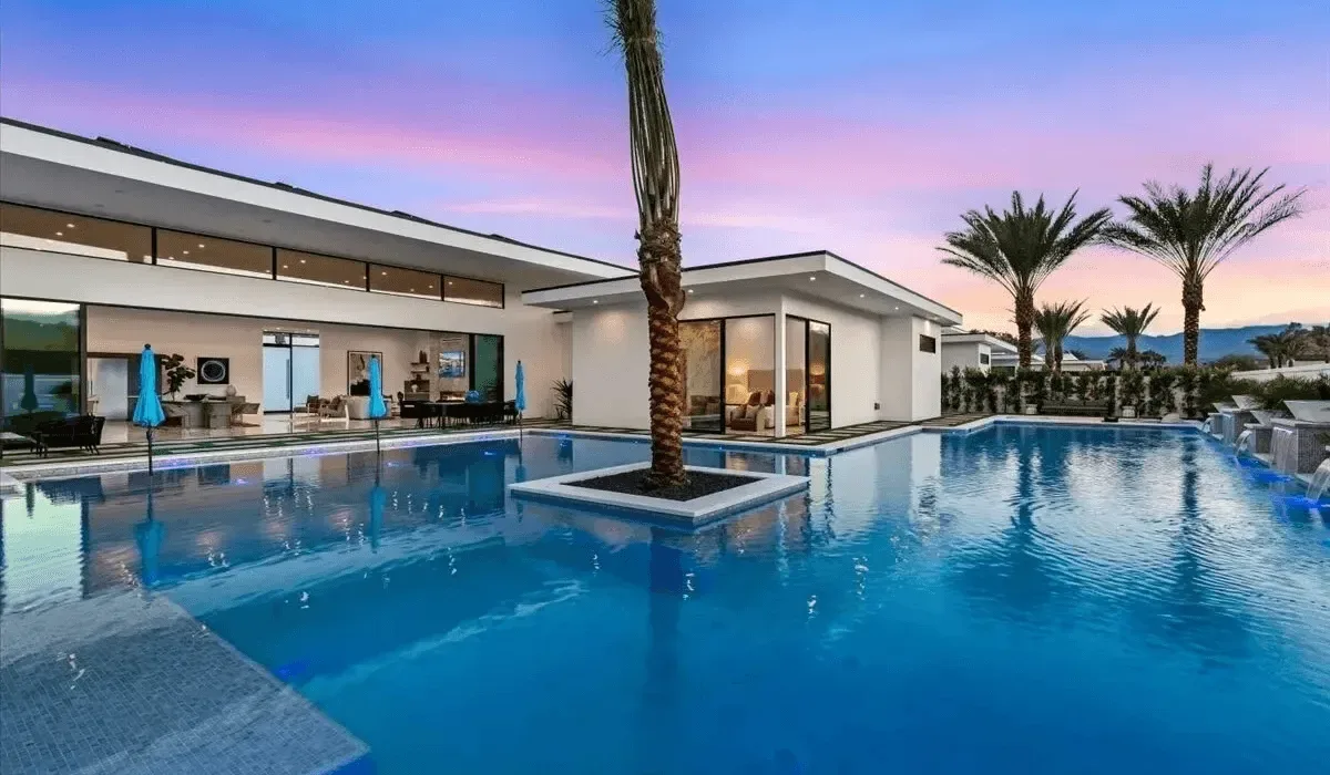 A modern house stands beside a large swimming pool at sunset.