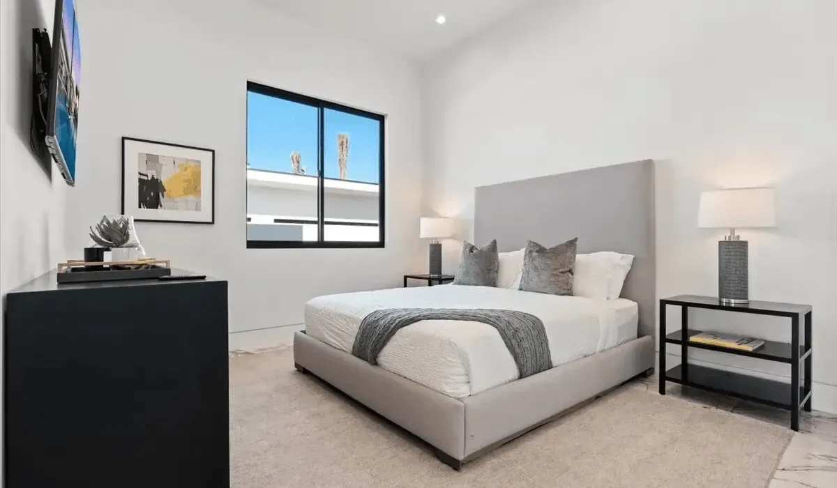 A bright bedroom with a neatly made bed and a large window.