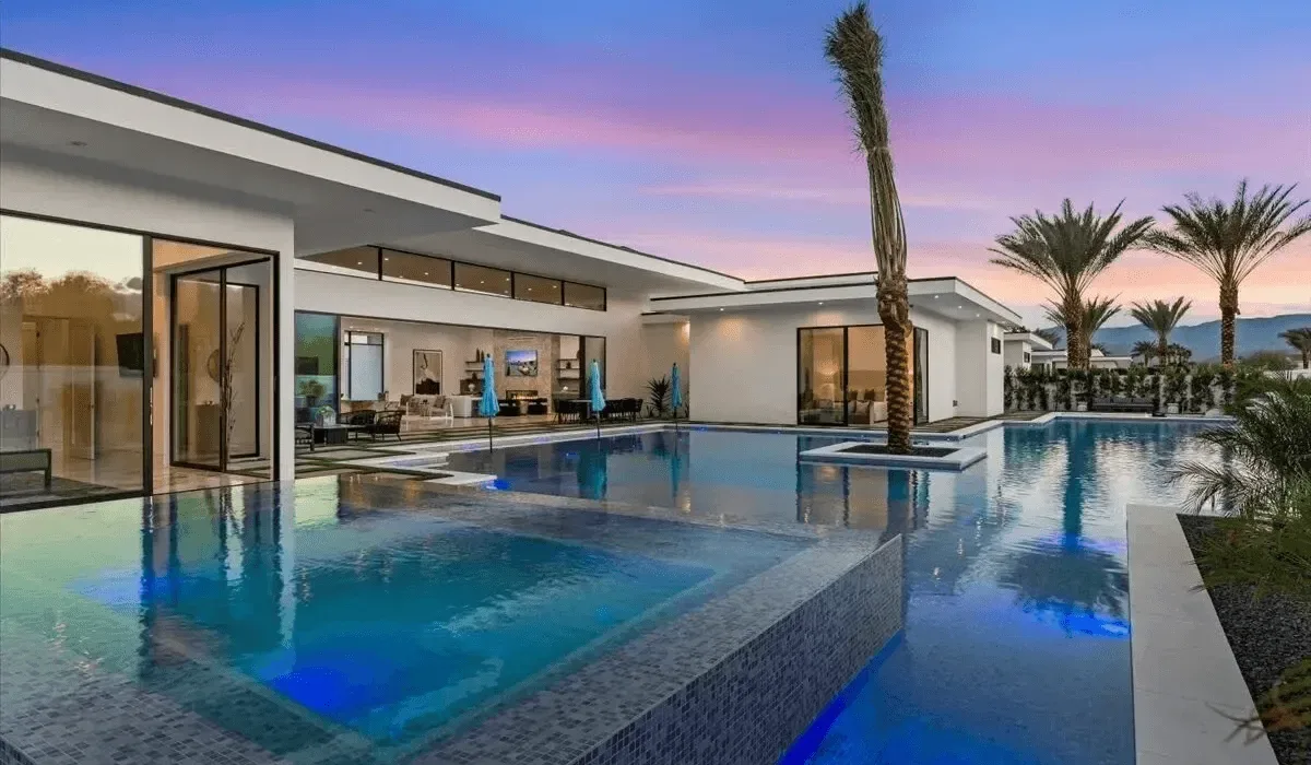A modern house opens onto a swimming pool beneath a colorful evening sky.