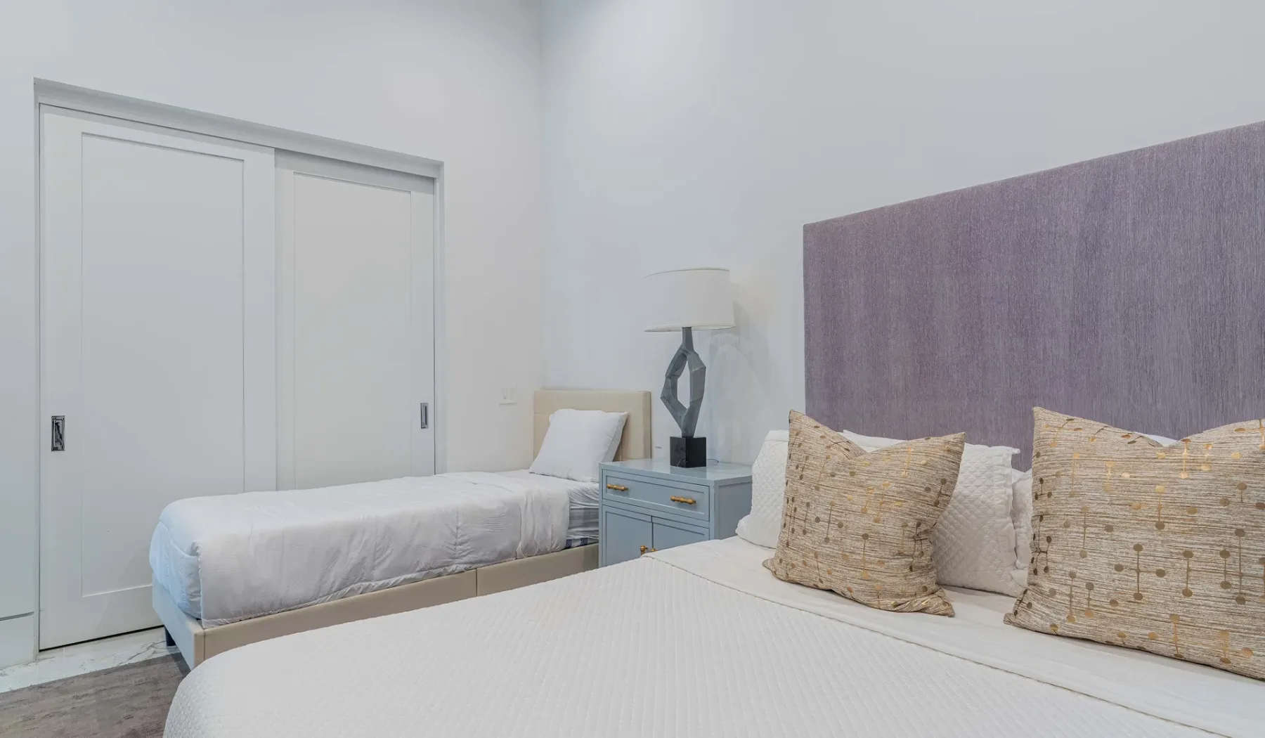 A bedroom with two beds, a bedside table, and a large upholstered headboard.