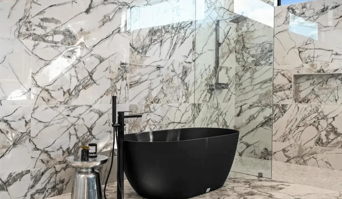 A freestanding bathtub sits in a bathroom with veined stone walls.