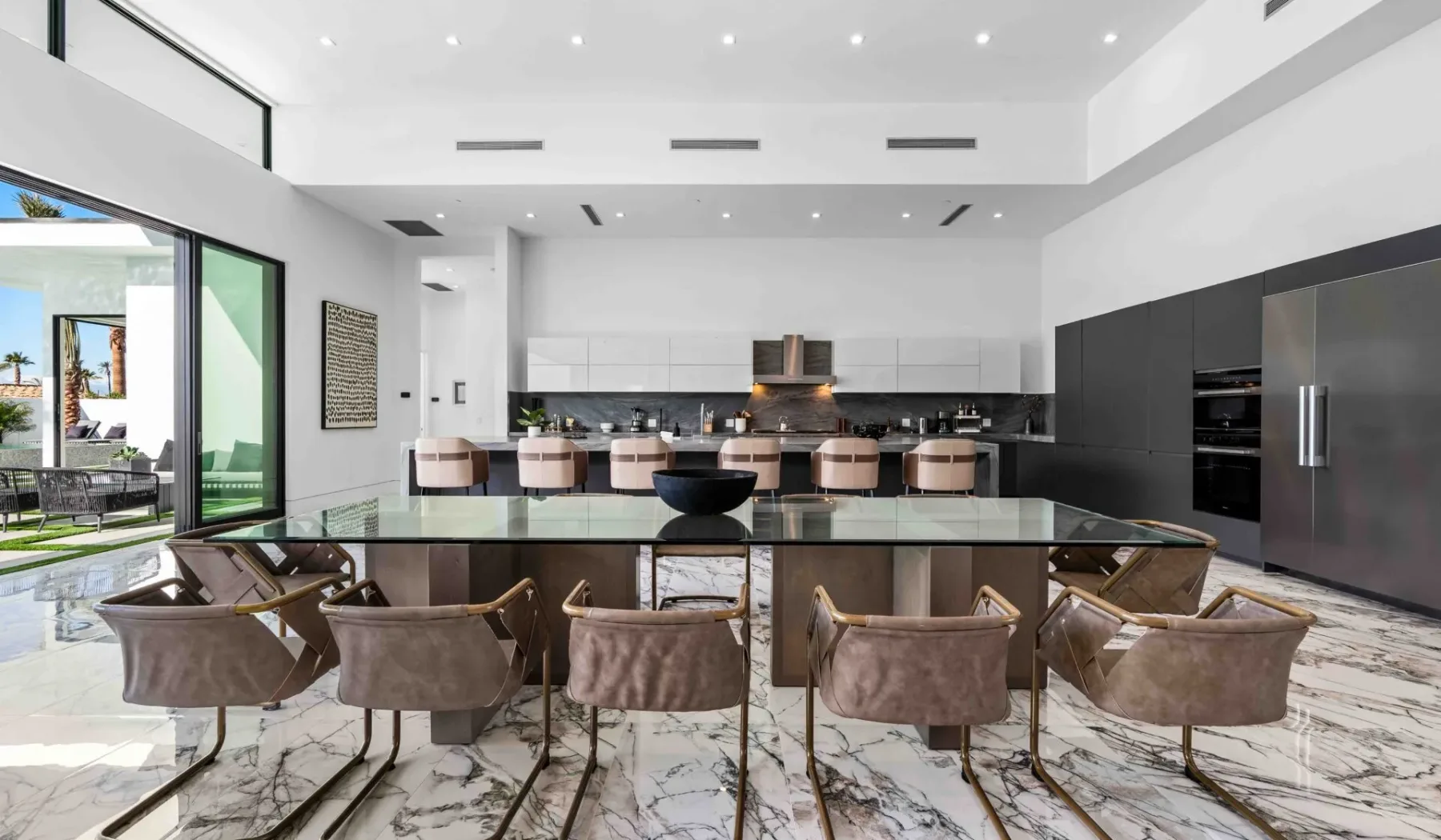 A modern kitchen and dining area with a long island and glass doors opening to a patio.