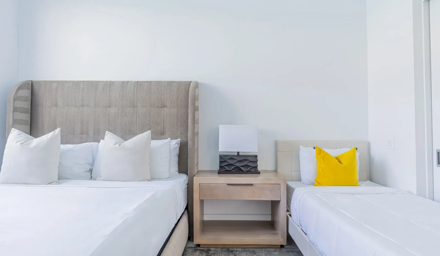 A bright bedroom with two beds and a nightstand between them.