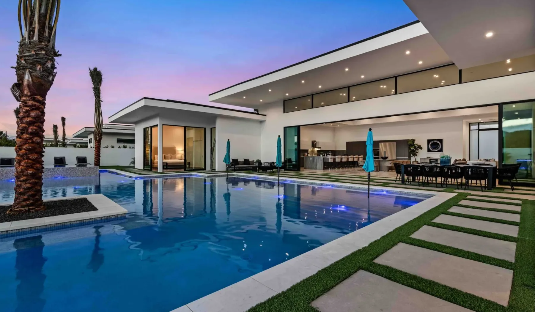 Modern house beside a swimming pool, with outdoor dining under a covered patio.