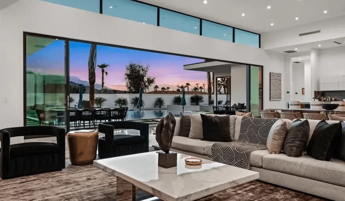 A modern living room opens onto a patio with a pool and sunset views.