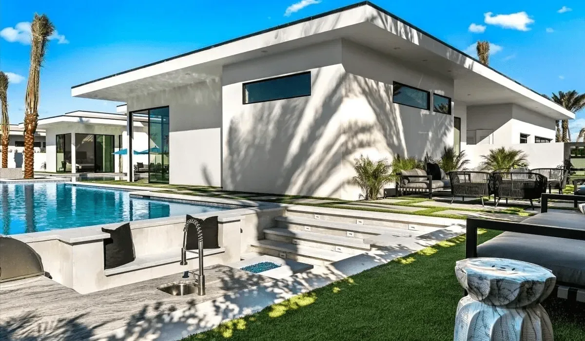 A modern white house overlooks a swimming pool and a small lawn.