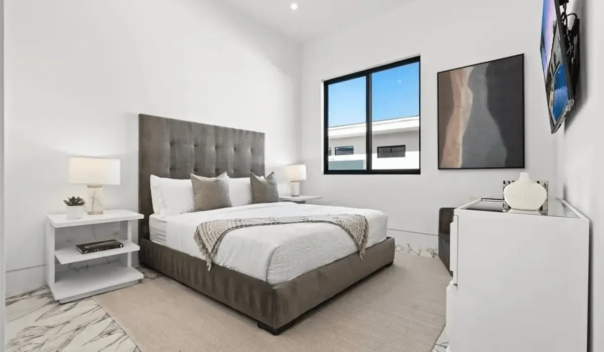 A modern bedroom with a large bed, bedside tables, and windows.