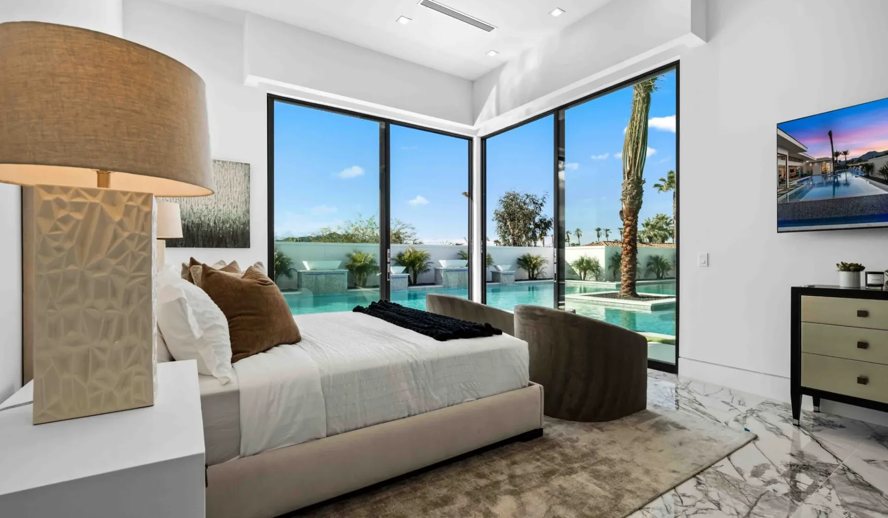 A bright bedroom with a bed beside large windows overlooking a pool.