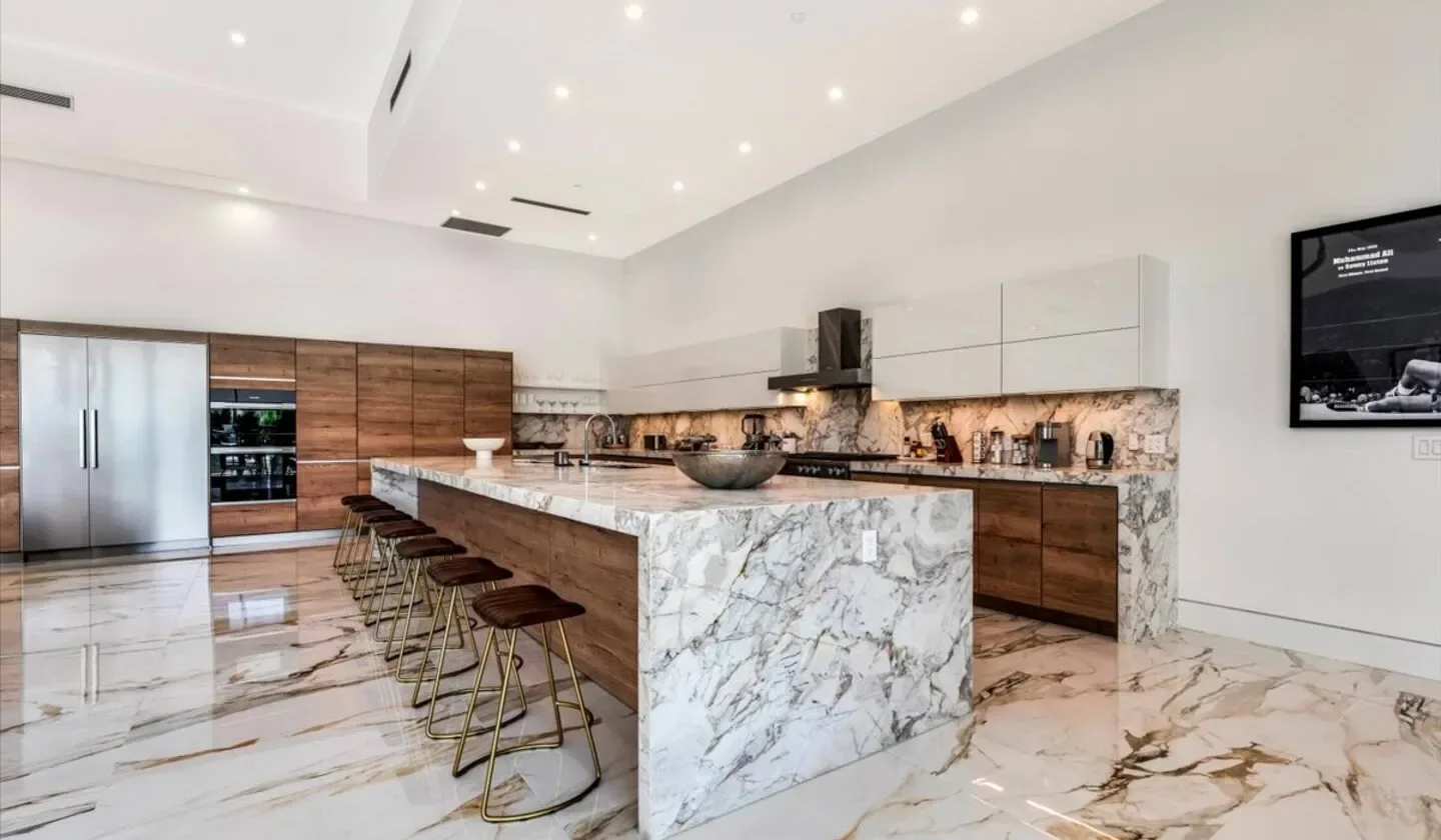 A spacious kitchen with a marble island, stools, and wood cabinetry.