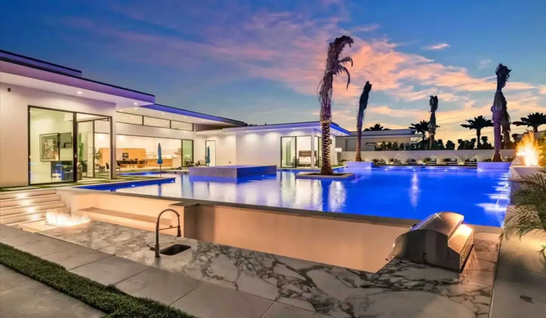 A modern house and illuminated swimming pool under a colorful evening sky.