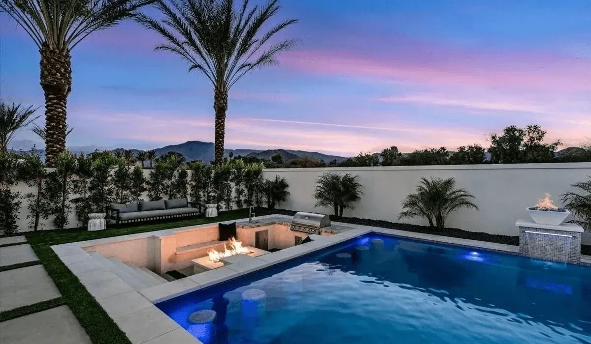 An outdoor swimming pool beside a sunken seating area at dusk.