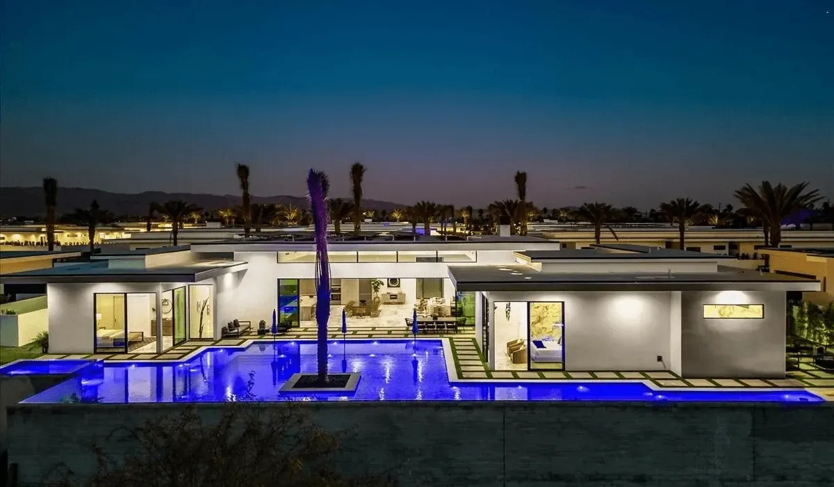 A modern single-story home at dusk, with a brightly lit swimming pool.
